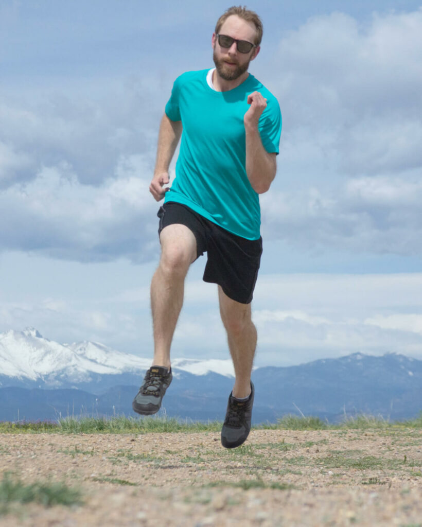 Man running on a trail with snow-capped mountains in the background
