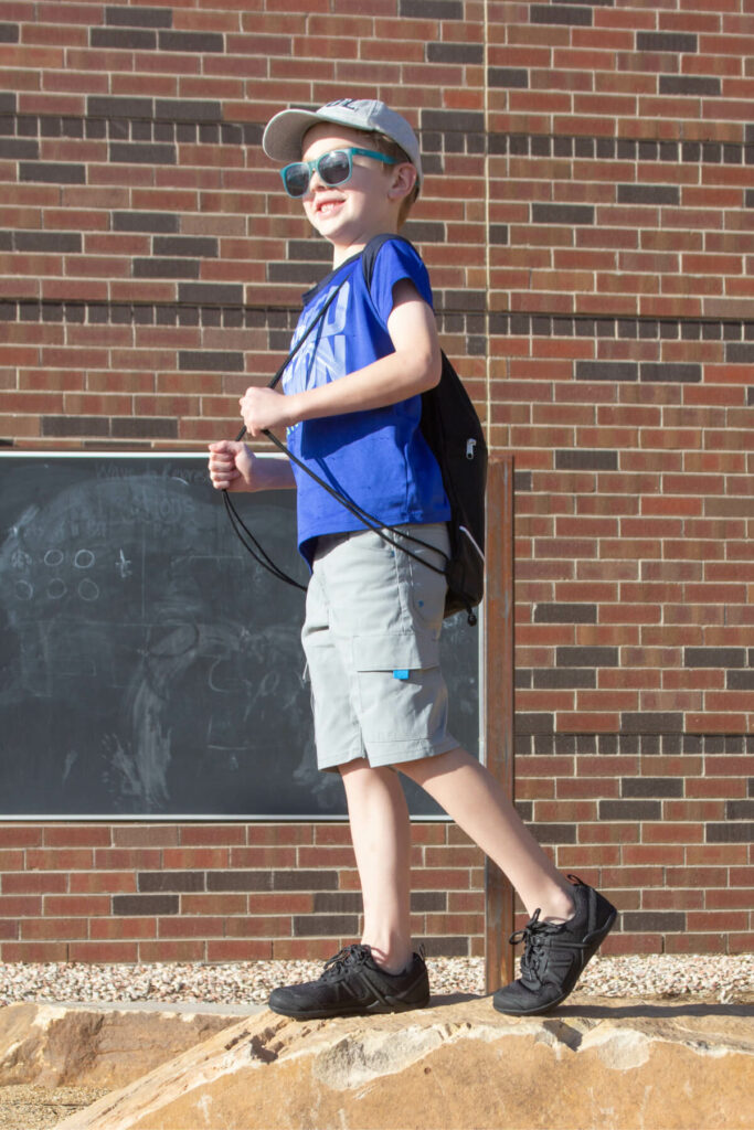 School-aged child wearing a backpack standing on a rock in front of a brick building