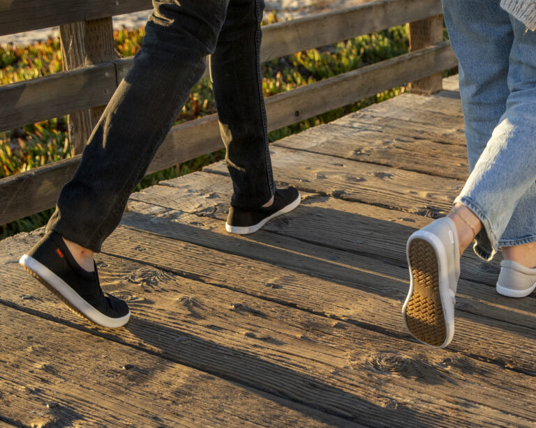 Two people wearing Dillon Canvas Slip-ons walking down the boardwalk at sunset