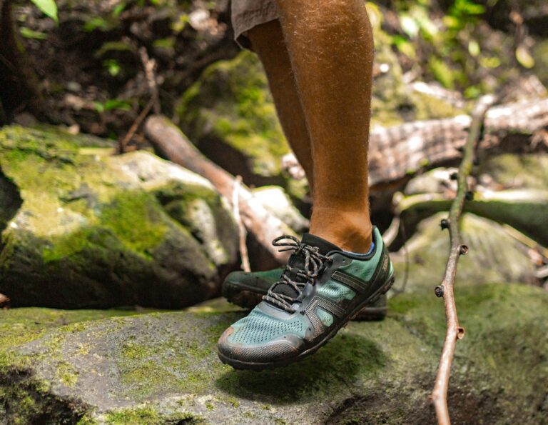 Knee-down view of a man wearing Mesa Trail II trail running shoes while standing on moss-covered rocks