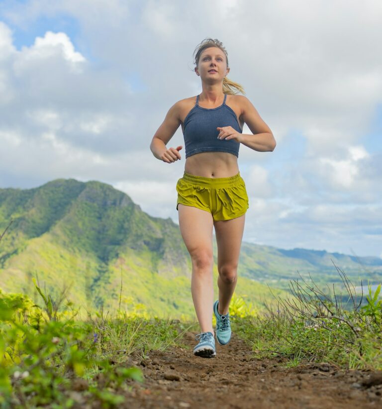 A woman wearing Mesa Trail II trail running shoes running on a dirt path with green hills behind her