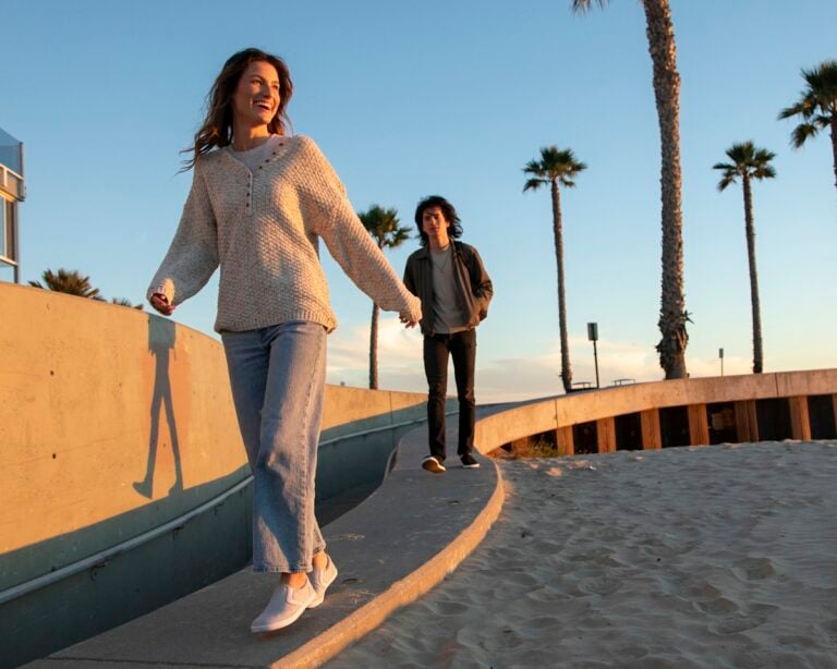 A woman and a man wearing Dillon Canvas Slip-ons smiling and walking towards the beach