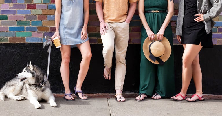 Four people leaning against a brick wall wearing sandals from Xero Shoes